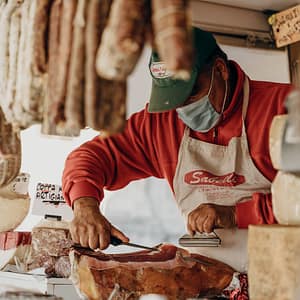 venditore di gastronomia che taglia una fetta di prosciutto artigianale